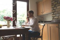Mann trinkt Kaffee, während er zu Hause Laptop benutzt — Stockfoto