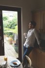 Uomo premuroso che prende il caffè mentre in piedi vicino alla finestra a casa — Foto stock