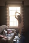 Visão traseira da mulher de pé perto da janela em casa — Fotografia de Stock