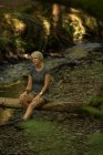 Woman relaxing on wooden log in the forest — Stock Photo