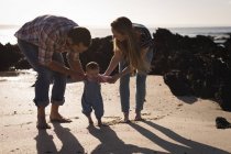 Родители учат ребенка ходить по пляжу в солнечный день — стоковое фото