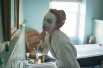 Жінка видаляє маску для обличчя перед дзеркалом у ванній вдома — стокове фото