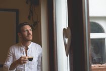 Удумливий чоловік має чорну каву, стоячи біля вікна вдома — стокове фото