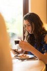 Bella donna che utilizza il telefono cellulare mentre prende il caffè a casa — Foto stock