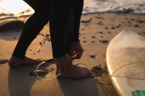 Крупный план сёрфера, привязавшего поводок для серфинга к ноге на пляже — стоковое фото