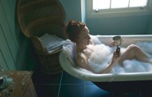 Woman using mobile phone in bathtub at bathroom — Stock Photo