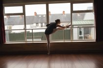 Ballerine s'étirant sur la barre tout en pratiquant la danse de ballet en studio de danse — Photo de stock