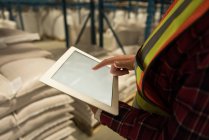 Section moyenne de travailleuse utilisant une tablette numérique à l'entrepôt — Photo de stock