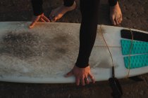 Primer plano de surfista recogiendo tabla de surf en la playa - foto de stock