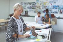 Female executive checking catalog on drafting table in office — Stock Photo