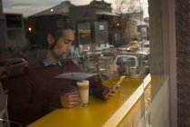 Человек с чашкой кофе с помощью мобильного телефона в кафе — стоковое фото