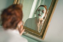 Жінка наносить маску для обличчя перед дзеркалом у ванній — стокове фото