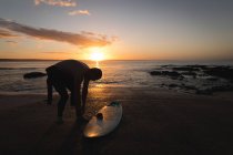 Surfista in costume sulla spiaggia durante il tramonto — Foto stock
