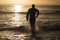 Surfeur avec planche de surf courant dans la mer au coucher du soleil — Photo de stock