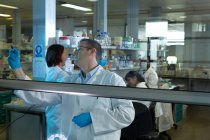 Équipe de scientifiques discutant sur panneau de verre en laboratoire — Photo de stock