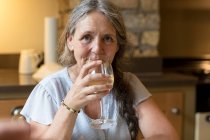 Retrato de una mujer mayor tomando vino en casa - foto de stock