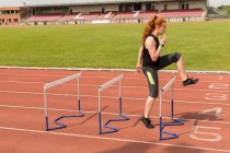Female athlete exercising over hurdles on running track — Stock Photo