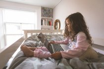 Девочка использует ноутбук на кровати в спальне дома — стоковое фото