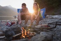 Couple roasting hot dog on campfire in mountains — Stock Photo