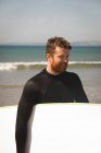 Surfista sonriente con tabla de surf caminando en la playa - foto de stock