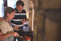 Счастливая пожилая пара готовит еду на кухне дома — стоковое фото