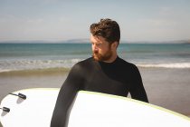Surfeur avec planche de surf marchant à la plage par une journée ensoleillée — Photo de stock
