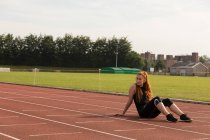 Jeune athlète féminine relaxante sur une piste de course — Photo de stock