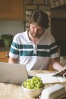 Hombre usando el ordenador portátil en la cocina en casa - foto de stock