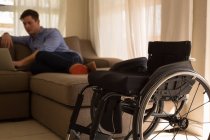 Hombre discapacitado usando el ordenador portátil en la sala de estar en casa - foto de stock