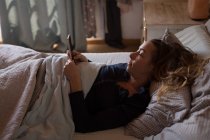 Frau benutzt Handy zu Hause im Bett — Stockfoto