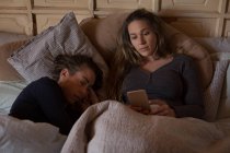Лесбиянки расслабляются и используют мобильный телефон на кровати дома — стоковое фото