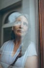 Mulher idosa atenciosa olhando através da janela em casa — Fotografia de Stock