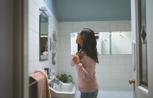 Woman combing hair front of mirror bathroom mirror at home — Stock Photo