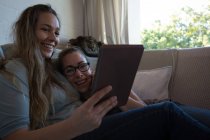 Casal de lésbicas usando tablet digital no sofá em casa — Fotografia de Stock
