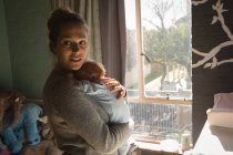 Mãe segurando bebê perto da janela em casa — Fotografia de Stock