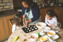 Бабушка с внучками готовят завтрак на обеденном столе дома — стоковое фото