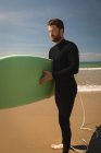 Серфер з дошкою для серфінгу стоїть на пляжі в сонячний день — стокове фото