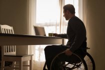 Disabled man having coffee while using laptop on dinning table at home — Stock Photo