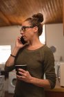 Крупним планом жінка з чашкою кави розмовляє на мобільний телефон вдома — стокове фото