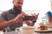 Мужчина фотографирует с мобильного телефона в кафе на открытом воздухе — стоковое фото
