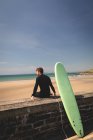 Vista laterale del surfista con tavola da surf seduta sulla parete circostante — Foto stock