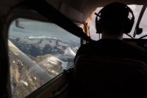 Rear view of pilot flying aircraft over snow covered mountain — Stock Photo