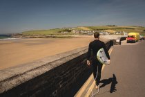Vista traseira do surfista com prancha andando na estrada — Fotografia de Stock