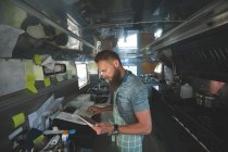 Camarero usando tableta digital mientras opera la máquina de facturación en camión de alimentos - foto de stock