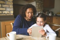 Abuela y nieta usando tableta digital en la cocina en casa - foto de stock