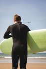 Rückansicht eines Surfers mit Surfbrett, der in Richtung Strand läuft — Stockfoto