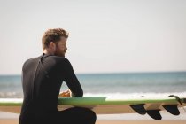 Surfer mit Surfbrett sitzt an einem sonnigen Tag am Strand — Stockfoto