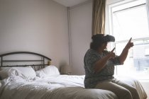 Пожилая женщина использует гарнитуру виртуальной реальности в спальне дома — стоковое фото