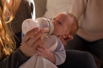 Close-up of mother feeding milk to baby on sofa at home — Stock Photo
