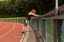 Young female athlete exercising on railing at sports track — Stock Photo